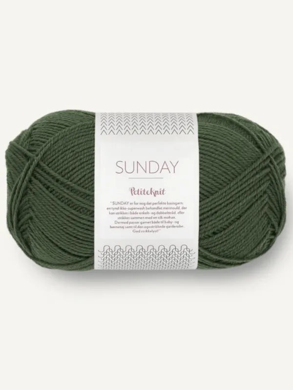 A skein of dark green Sandnes Garn Sunday yarn with a white label featuring stitching patterns, mulesing-free info, and multilingual details.