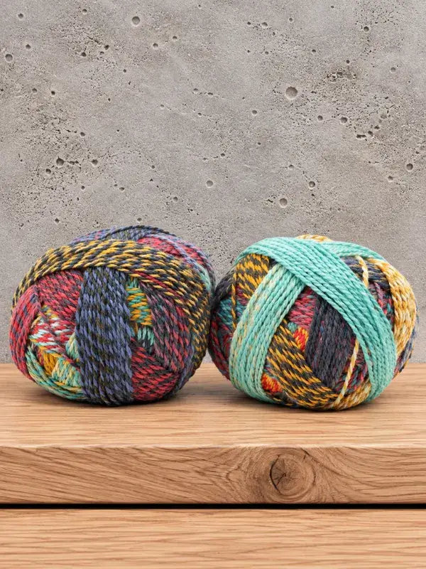 Two round skeins of Schoppel-Wolle Edition 3 multicolored yarn in shades of blue, red, yellow, and teal.