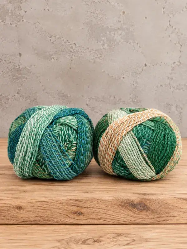 Two balls of Schoppel-Wolle Edition 3 yarn in variegated shades of green, light mint, and cream.