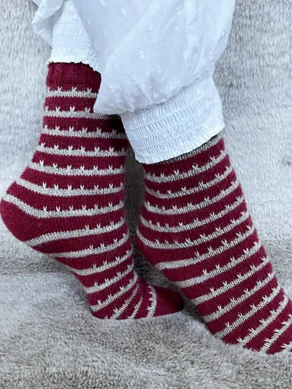 Timo sukka ohje fingerin ja Lang jawoll knitted socks with a pattern of dark red and light grey stripes featuring small vertical stitch details, crafted from fingering weight yarn.