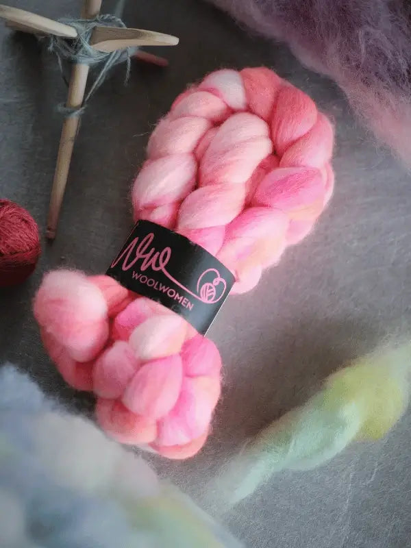 Two bundles of WoolWomen kehruukuitu Corriedale käsinvärjätty in pink, white, peach, and magenta. Ideal for kehräämiseen. Each bundle features a "Woolwomen" label and is displayed on a textured gray surface.