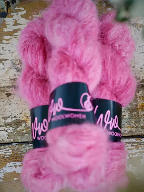 Two skeins of bright pink, fuzzy WoolWomen Fluff Mohair wrapped in black paper bands.
