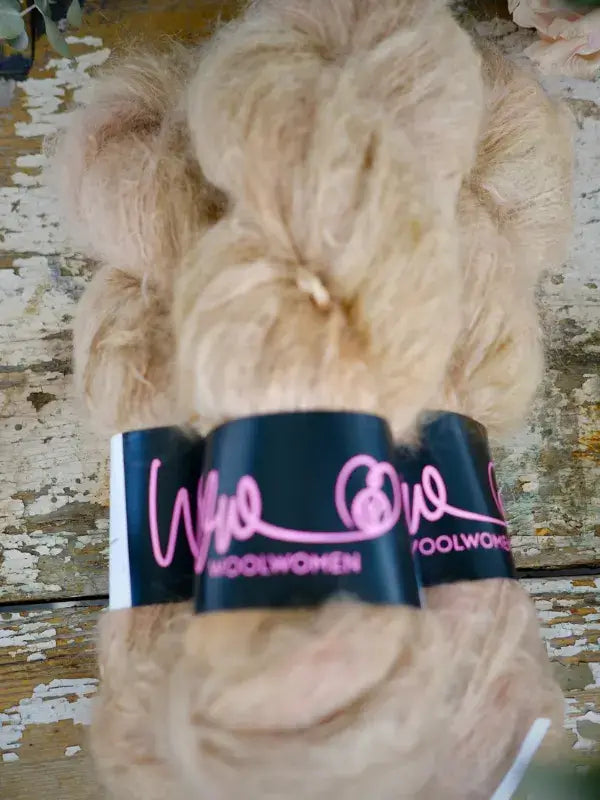 A skein of WoolWomen Fluff Mohair in fluffy, light beige with a black paper label.