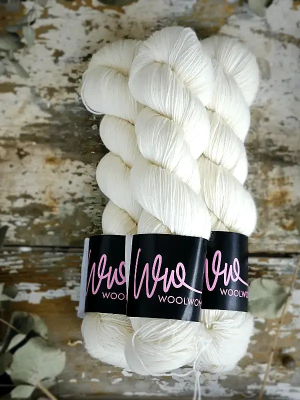 Three twisted hanks of cream-colored WoolWomen Merino Sock yarn bound together by black paper labels.