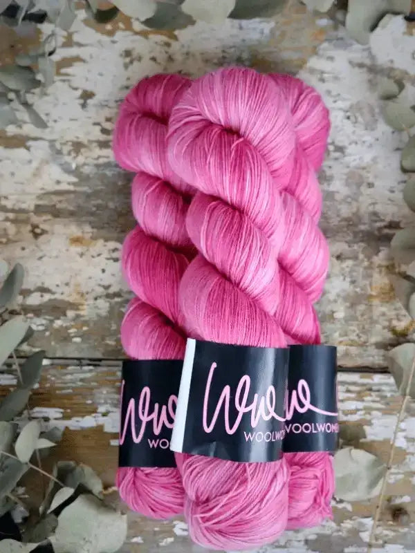 Two skeins of bright pink hand-dyed WoolWomen Merino Sock yarn twisted together with a black paper label.