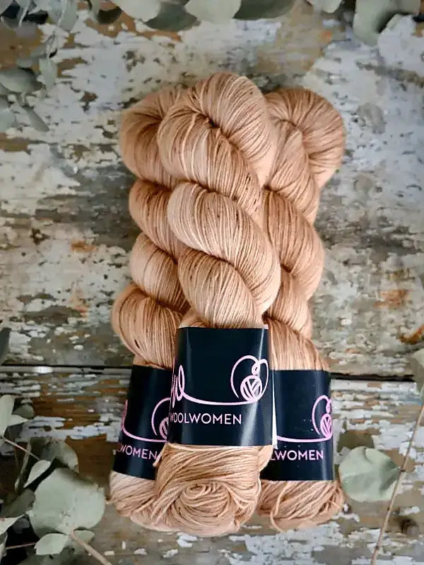 Two twisted hanks of light tan WoolWomen Merino Sock yarn secured by black paper bands.