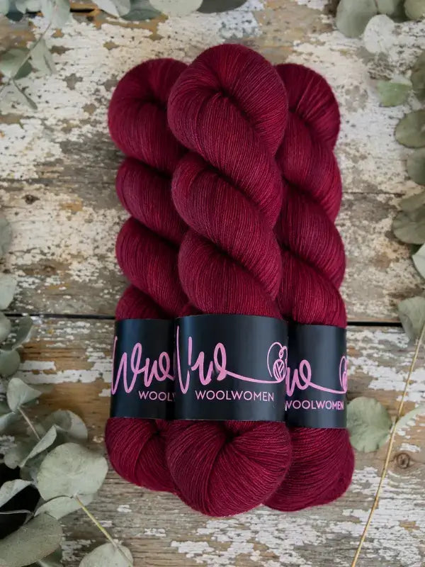 Three skeins of deep red WoolWomen Merino Sock yarn wrapped in black labels.