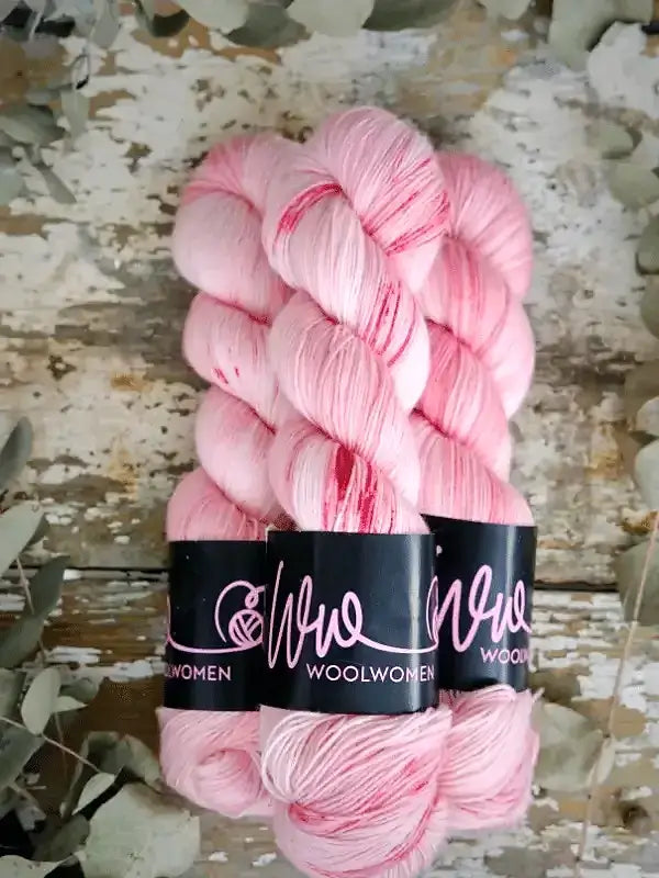 Three skeins of WoolWomen Merino Sock yarn in pale pink with darker pink speckles, bundled together with black paper labels.