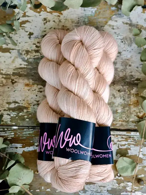 Two skeins of pale pink WoolWomen Merino Sock yarn with black paper labels.