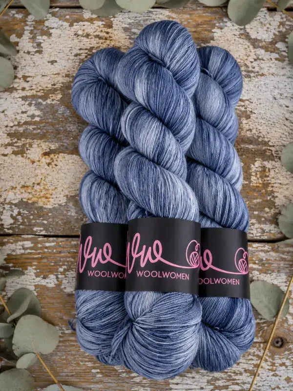 Three skeins of WoolWomen Merino Sock yarn in blue and white variegated colors with black labels.