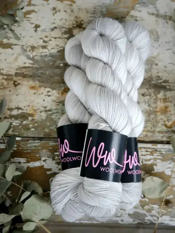 Two skeins of soft, light gray WoolWomen Merino Sock yarn tied with branded paper labels.
