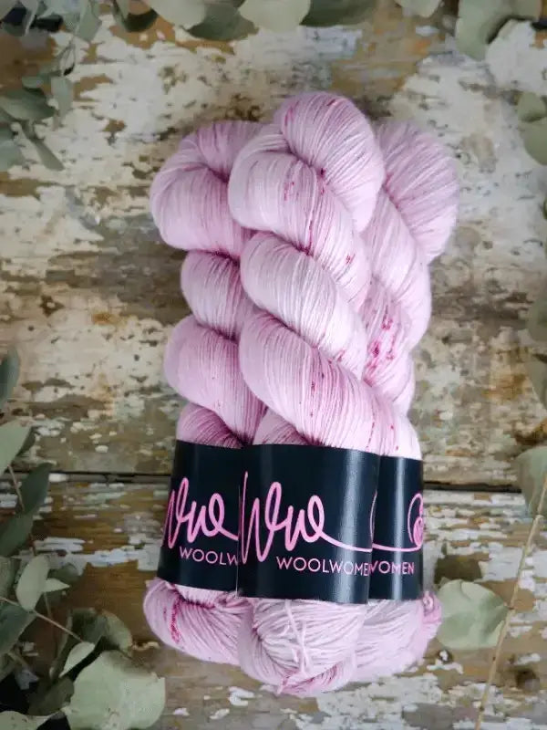 Two skeins of pale pink WoolWomen Merino Sock yarn with darker speckles, held together by a black paper label.