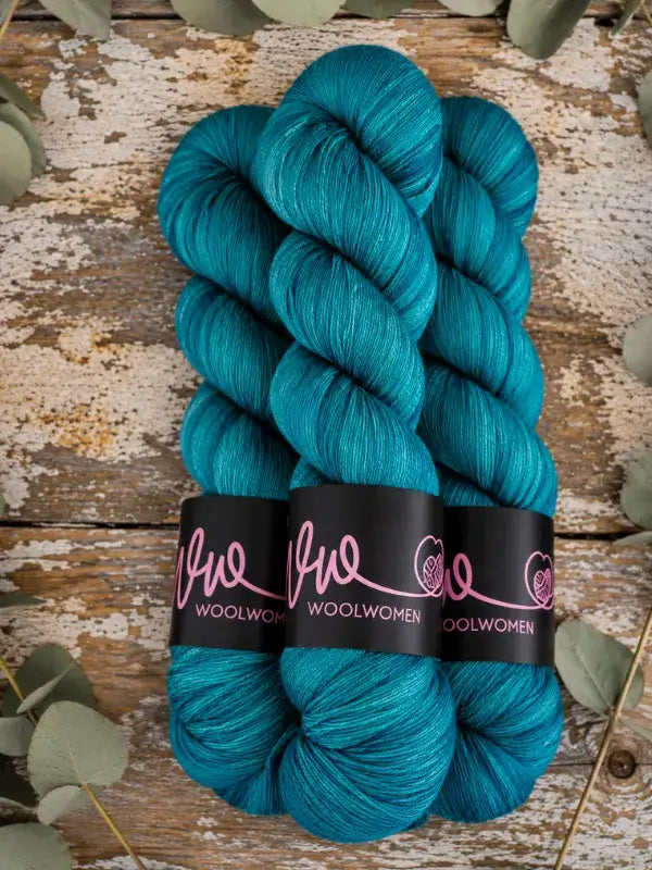 Three hanks of teal, hand-dyed WoolWomen Merino Sock yarn with black paper labels.