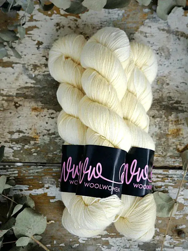 Two skeins of cream-colored WoolWomen Merino Sock superwash merinovilla yarn bound with black paper labels.