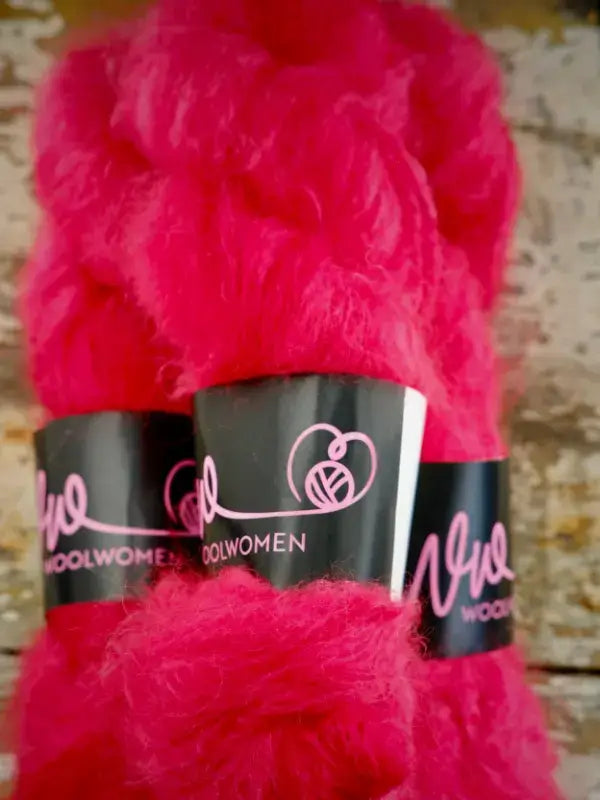 A skein of bright pink fluffy WoolWomen Fluff Mohair yarn with black product labels.