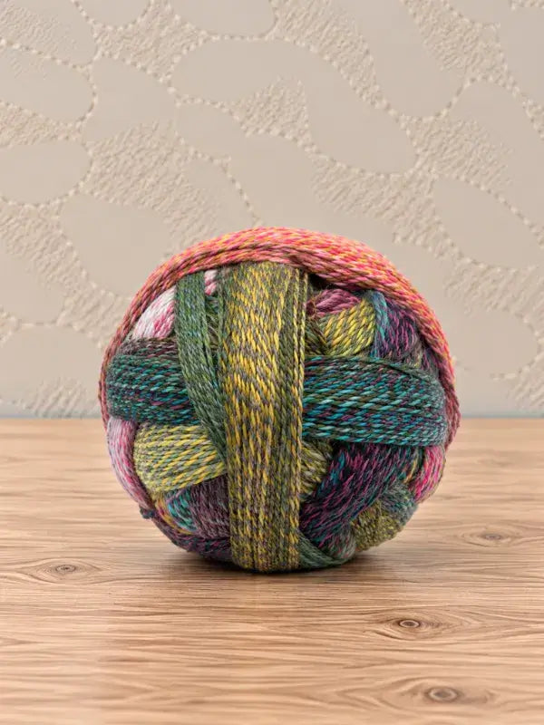 A ball of Schoppel wolle Zauberball crazy yarn featuring variegated shades of green, yellow, pink, and purple.