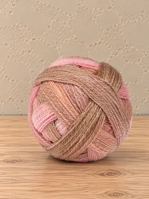 A ball of Schoppel wolle Zauberball crazy yarn in variegated shades of pink, peach, and brown.