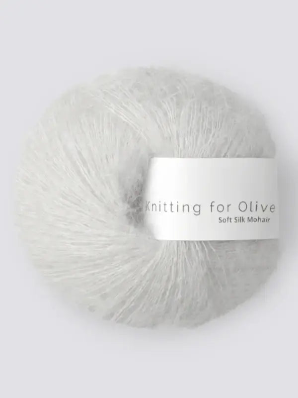 A ball of soft, light gray Knitting for Olive Soft Silk Mohhair yarn with a white label, spun from Kid mohair lanka and silkki lanka in accordance with the Responsible Mohair Standard, rests against a plain, light background.