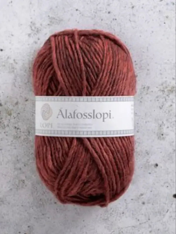 A skein of reddish-brown Istex Alafosslopi yarn, crafted from genuine Icelandic wool, with a white label sits on a speckled gray surface.