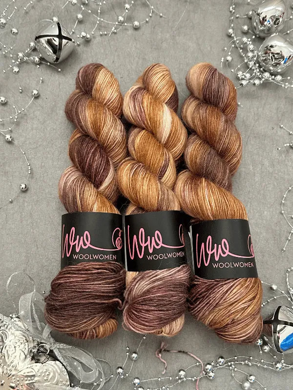 Three skeins of WoolWomen Alpaca Sock -yhden padan ihmeet in variegated brown, tan, and cream are arranged side by side on a gray surface, surrounded by silver beads, string, and festive decorations—ideal for lämmin sukalanka projects.