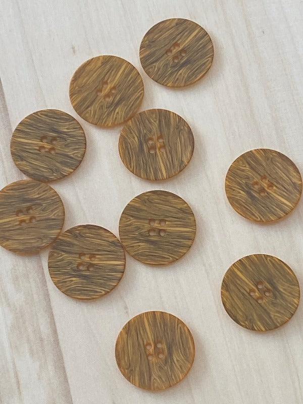 Ten Muovinappi 23mm round, brown buttons with a woodgrain pattern and two holes each are scattered on a light wooden surface. These lightweight buttons are ideal for various projects and come in different colors to match your style.