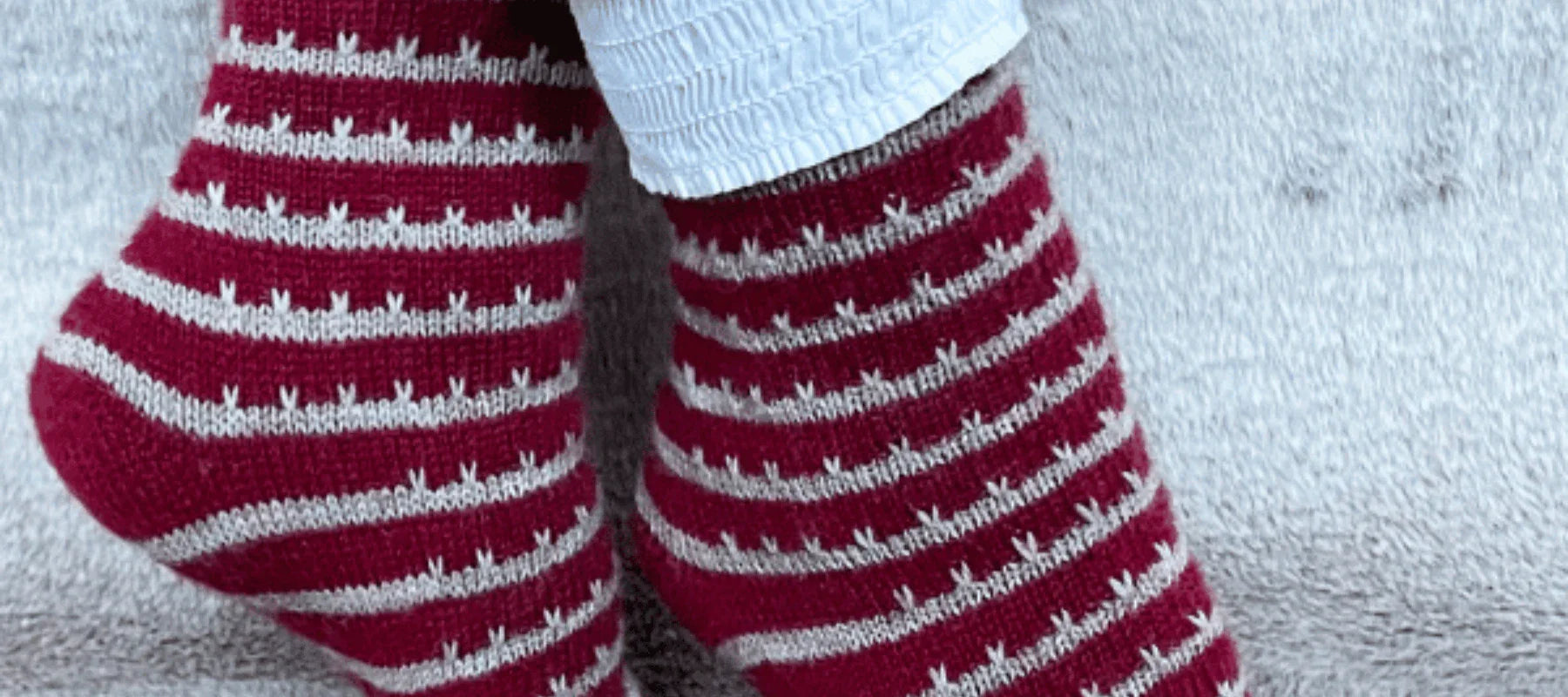 Close-up of two feet wearing red and white striped knit socks, with white pants, resting on a light grey textured surface.