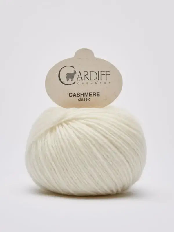 A ball of soft, white Cardiff Cashmere Classic – 100% kashmirlanka yarn with its label is displayed against a plain light background.