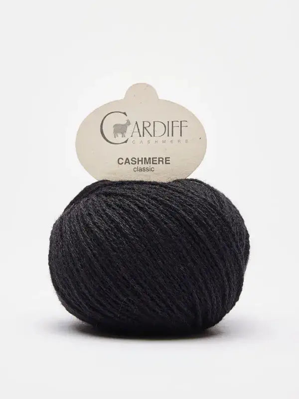 A ball of dark gray Cardiff Cashmere Classic – 100 % kashmirlanka rests against a white background, its product label displayed on top and highlighting the luxurious quality of this premium cashmere yarn.
