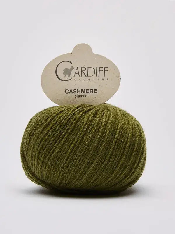 A ball of Cardiff Cashmere Classic – 100% kashmirlanka yarn in olive green, with its label inserted on top, displayed against a plain white background.
