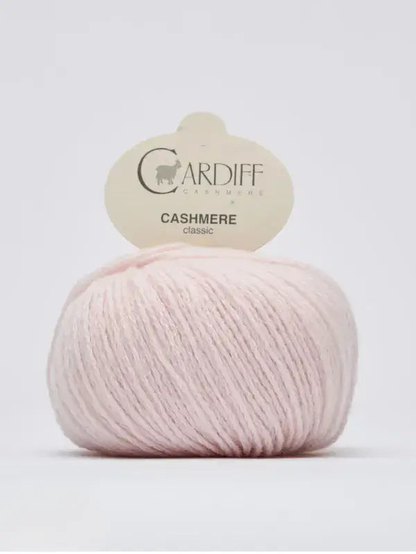 A ball of light pink Cardiff Cashmere Classic – 100 % kashmirlanka yarn, renowned for its luxurious Italian cashmere quality, with a label on top against a plain white background.