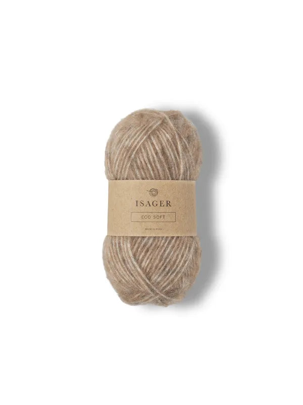 A skein of light brown Isager Soft is displayed on a plain white background. The beige label features elegant text and highlights the luxurious softness of this premium knitting yarn.
