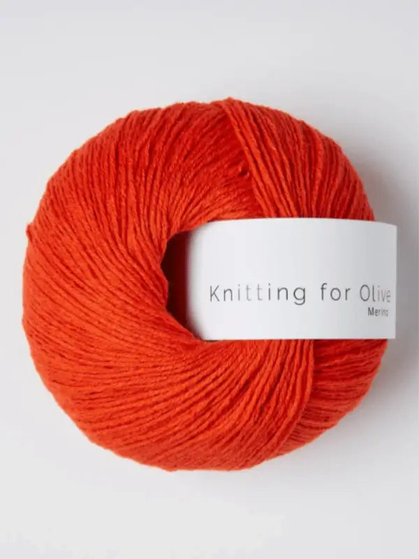A ball of vivid orange Knitting for Olive Merino yarn with a white label lies on a plain light background. This merino wool is Öko-Tex certified, ensuring quality and safety for your knitting projects.