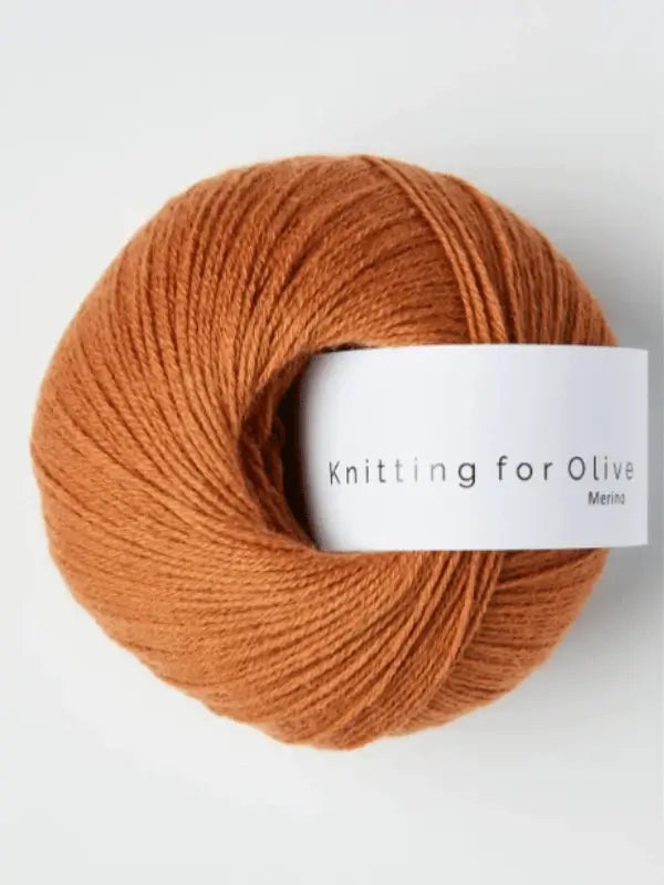 A warm brown ball of Knitting for Olive Merino yarn with a white label, Öko-Tex certified, is photographed on a light background.