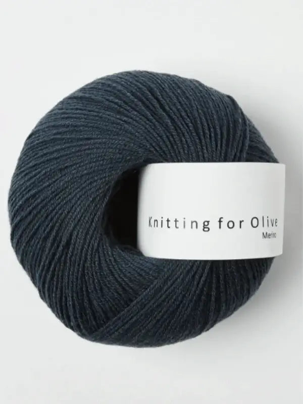 A ball of dark blue Knitting for Olive Merino yarn with a white label is displayed on a plain light background.