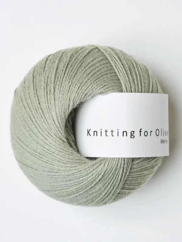 A ball of soft, smooth sage green Knitting for Olive Merino yarn with a white label, Öko-Tex certified and neatly wound—perfect for cozy knitting projects.