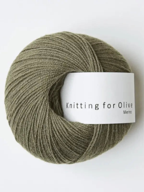A ball of olive green Knitting for Olive Merino yarn with a white label rests against a plain light background.
