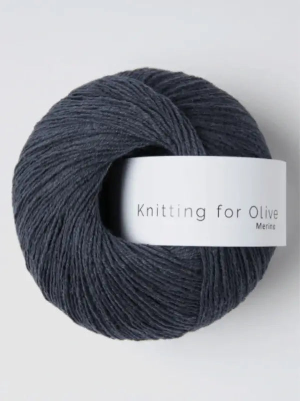 A ball of dark gray Knitting for Olive Merino yarn sits on a light, neutral background, its white label visible.