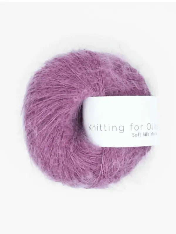 A ball of fluffy, mauve-colored yarn—crafted from vastuullinen mohair and kid mohair lanka—featuring a white label that displays the product name, Knitting for Olive Soft Silk Mohair, rests on a plain white background.