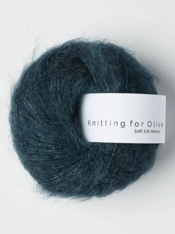 A ball of Knitting for Olive Soft Silk Mohair yarn in dark teal, made from kid mohair and silkki lanka, with a white label displaying the product name, set against a plain light background.