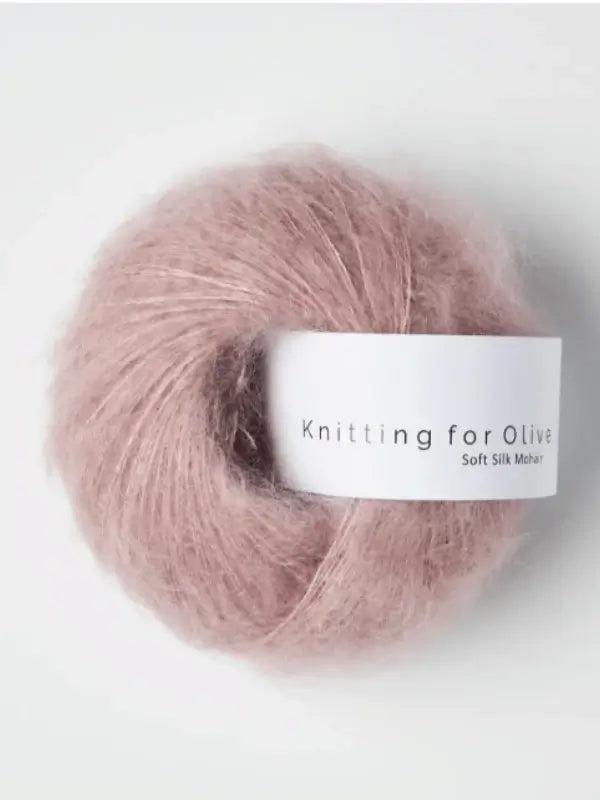 A ball of Knitting for Olive Soft Silk Mohair in dusty pink, made from fibers that meet the Responsible Mohair Standard, rests on a white surface.