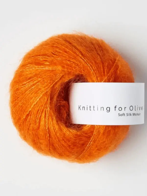 A skein of vibrant orange Knitting for Olive Soft Silk Mohair yarn, made according to the Responsible Mohair Standard, features a white label with the product name and is set against a plain white background.