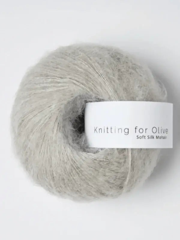 A ball of Knitting for Olive Soft Silk Mohair in light gray, made from luxurious kid mohair and silkki lanka, features a white label with the brand name and rests against a plain white background. This yarn is produced in accordance with the Responsible Mohair Standard.
