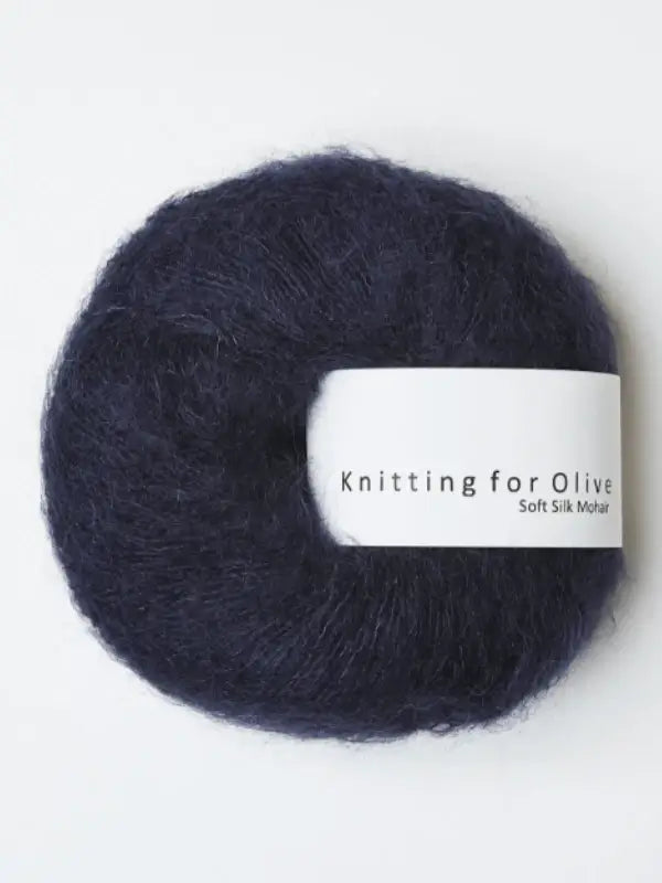 A deep navy blue ball of Knitting for Olive Soft Silk Mohhair yarn, spun from premium kid mohair and silk, features a white label with the brand name wrapped around it. This silkki lanka adheres to the Responsible Mohair Standard, guaranteeing quality and sustainability.