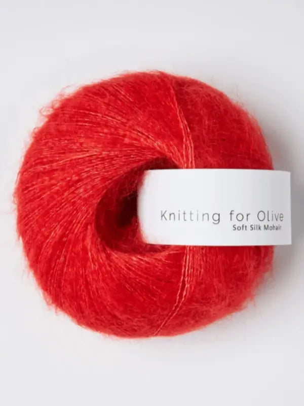 A vibrant red ball of Knitting for Olive Soft Silk Mohair yarn rests on a white surface.