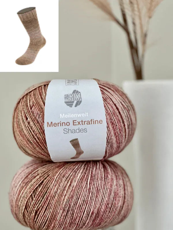 Two skeins of Lana Grossa Meilenweit 100 Merino extrafine Shades in pinkish-brown are stacked in front of a white vase with dried plants. An inset shows a knitted sock made from the same soft, mulesing-free merino yarn.