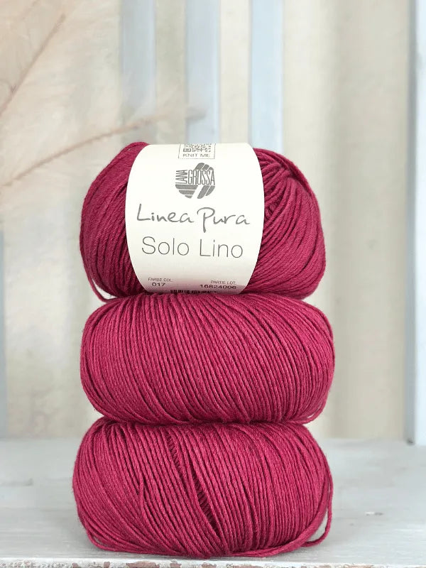 Three skeins of Lana Grossa Solo Lino, in deep pink, are stacked vertically with the label on the top skein. This vegan yarn is set against a light, softly textured background.