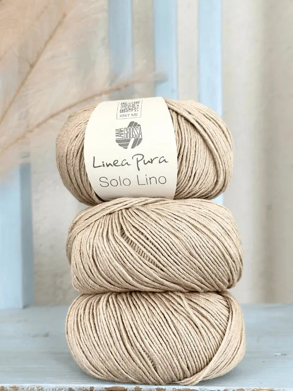 Three beige balls of Lana Grossa Solo Lino, a vegan yarn, are stacked vertically. The top ball's label reads Linea Pura Solo Lino. The yarn is placed on a light blue wooden surface with a gentle background.