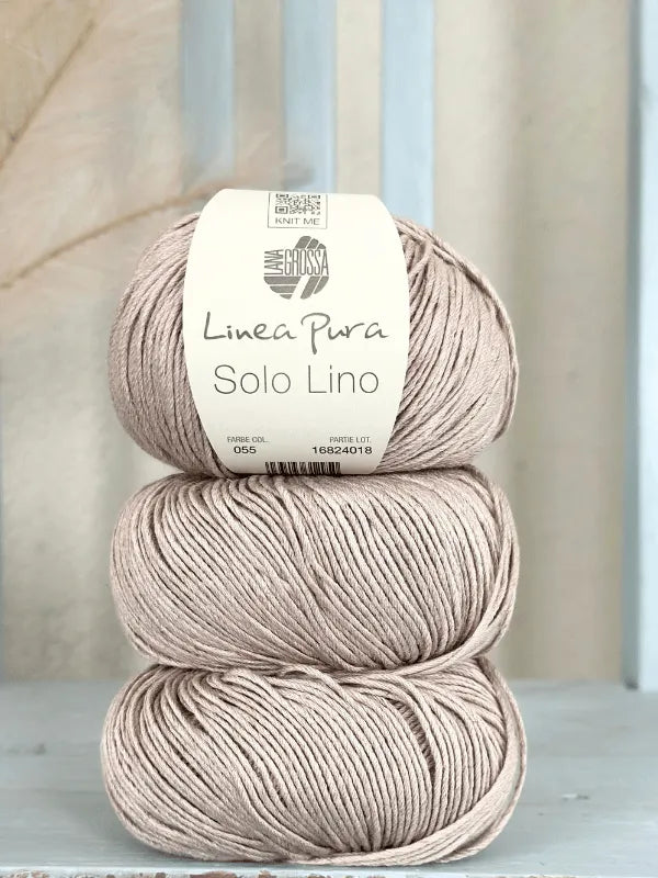 Three balls of beige pellavalanka are stacked on a light blue wooden surface. The top ball is labeled Lana Grossa Solo Lino, showing additional product details.