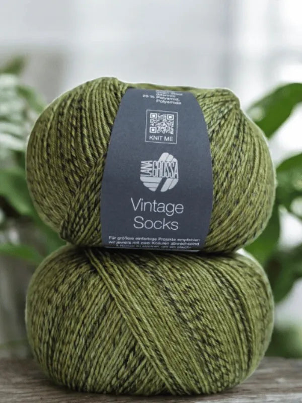 Two skeins of Lana Grossa Vintage socks yarn are stacked together, with blurred green leaves in the background—an inspiring scene for your Lauri Fingerin sukkaohje +Lana Grossa Vintage socks project.