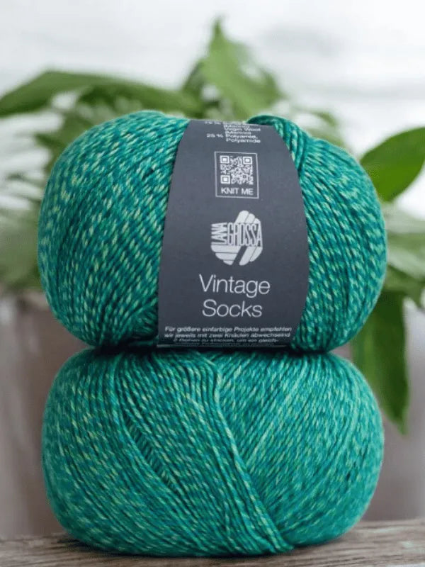 Two skeins of Lana Grossa Vintage Socks yarn labeled "Knit Me," stacked with a leafy backdrop—perfect for making villasukat or using the Lauri Fingerin sukkaohje +Lana Grossa Vintage socks pattern.
